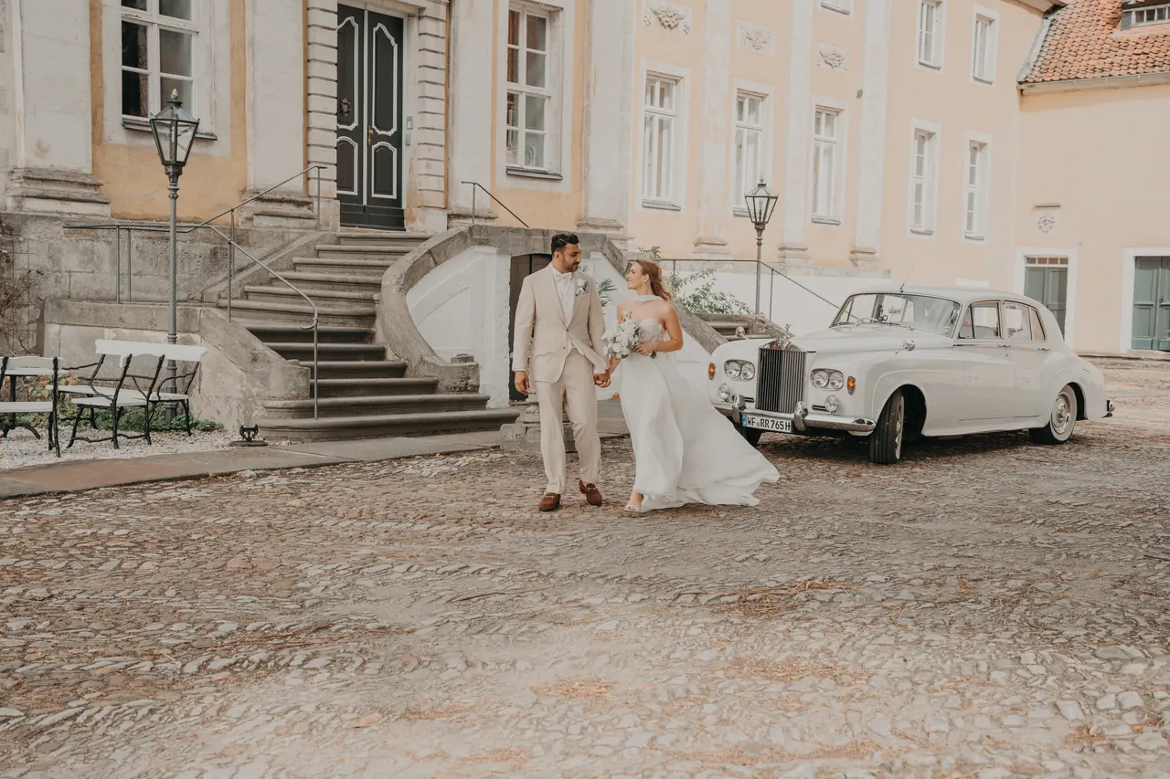 Brautpaar vor einem Schloss mit einem weißen Oldtimer von Love of Driving