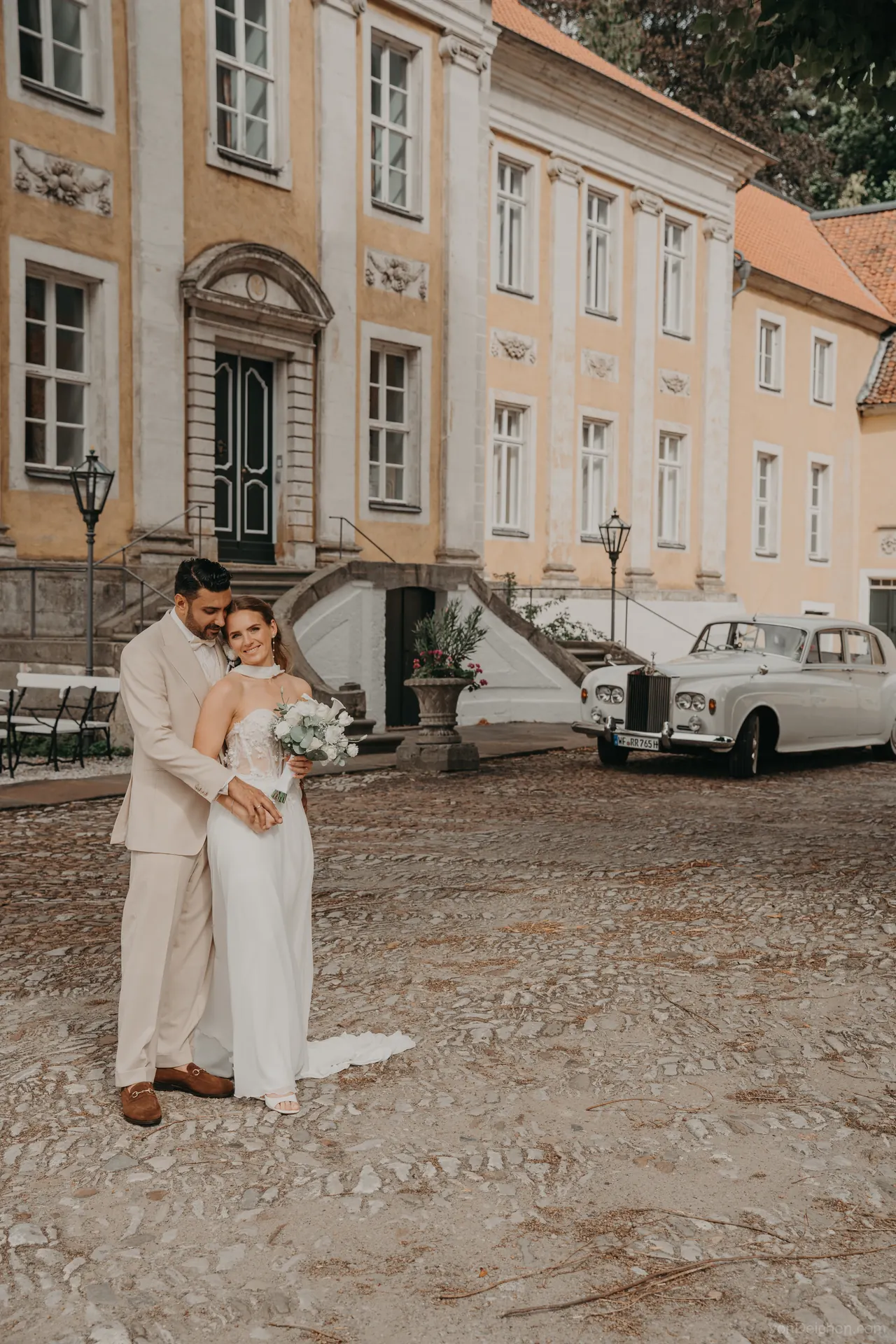 Brautpaar vor einem Schloss mit weißem Oldtimer