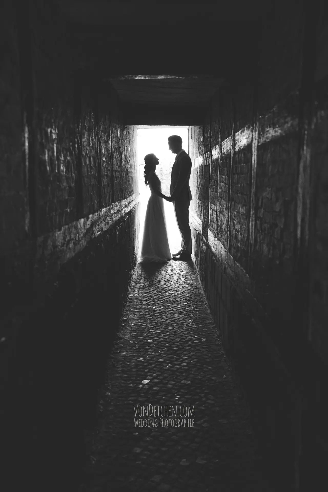 Brautpaar als Silhouette am Ende eines dunklen Tunnels, schwarzweiß